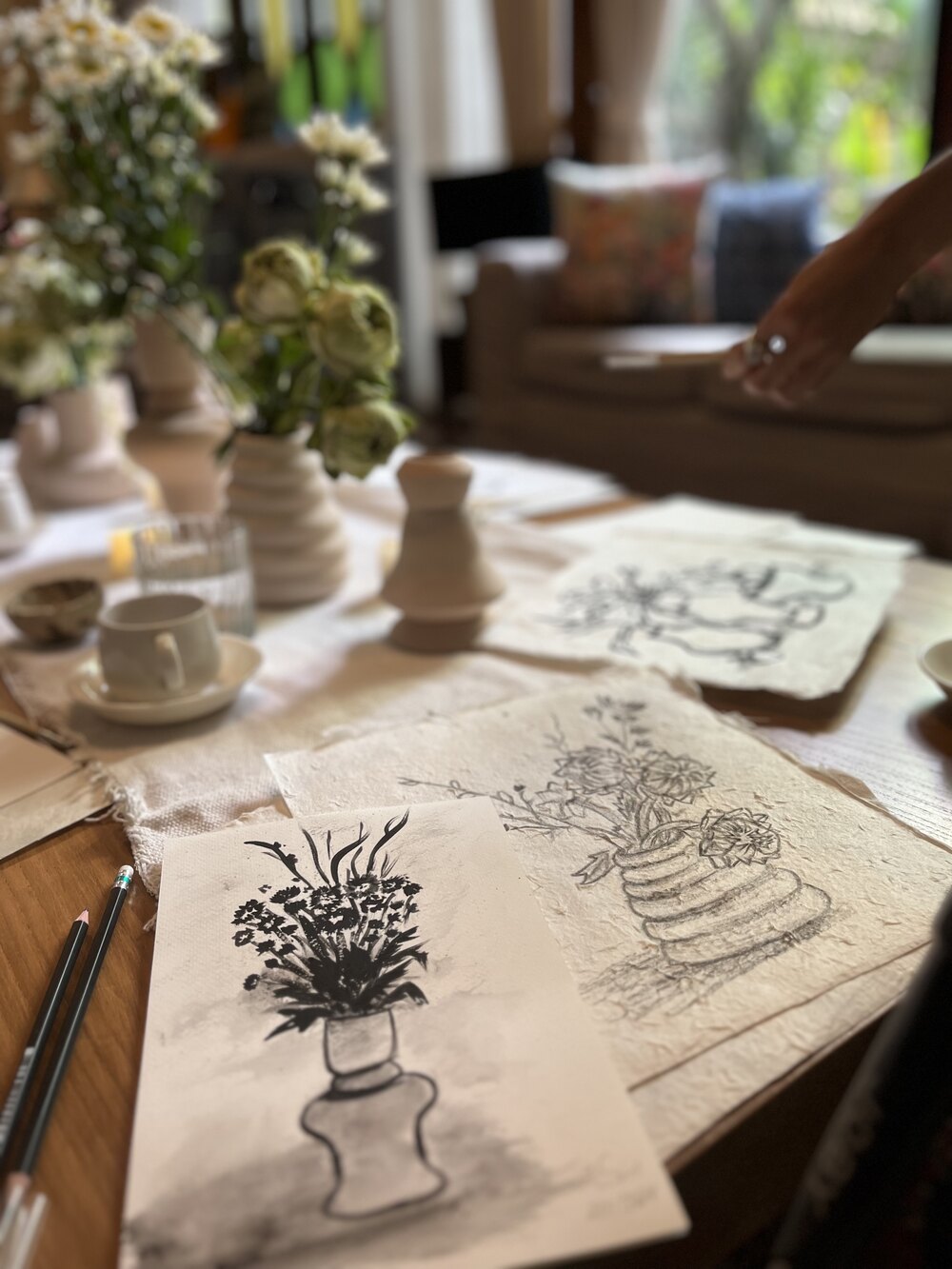 Flower sketches, drawing pencils, ceramics, and a cup on a wooden table.